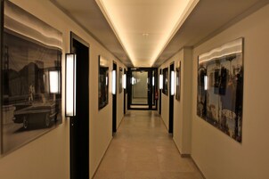 Un pasillo de hotel con obras de arte enmarcadas en las paredes, piso de baldosas y una lámpara en el techo.
