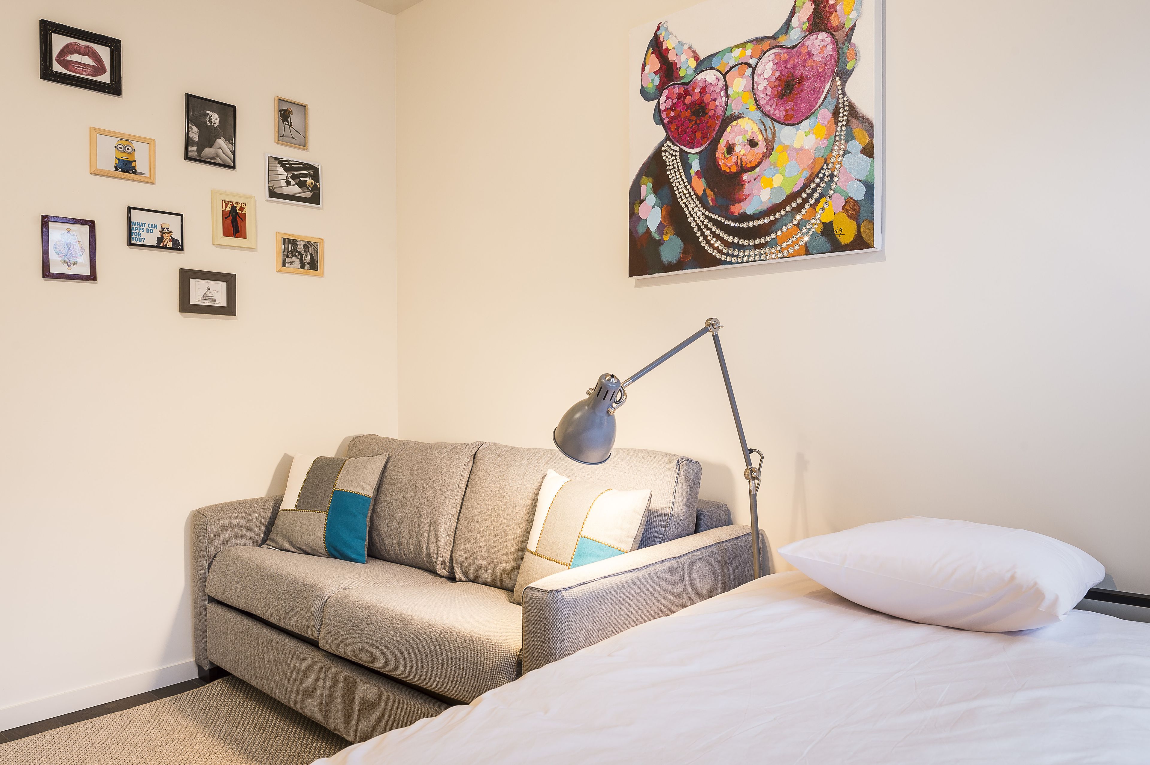 A bedroom with a bed, a desk with a lamp, a sofa, and a wall with framed pictures.