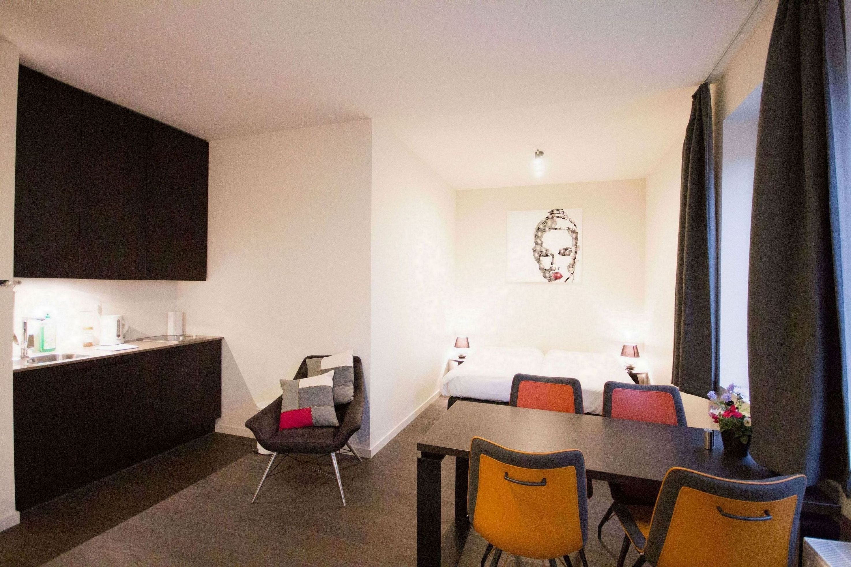 Una habitación de hotel moderna con zona de comedor, kitchenette y una cama grande.