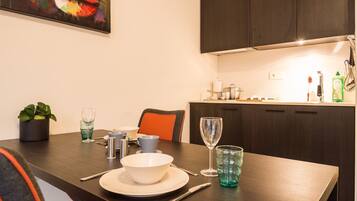 Un coin repas avec une table dressée pour deux personnes, une plante en pot et un tableau accroché au mur.