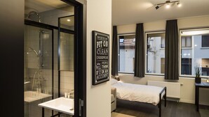 A modern hotel room with a shower, a bed, a bedside table, and a window with curtains. - Getaway Leuven (Leuven)