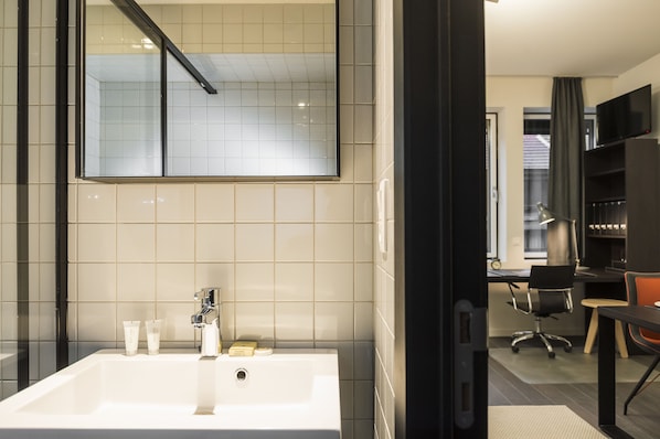 Un baño moderno con un espejo grande, azulejos blancos, un lavabo blanco y artículos de aseo.