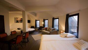 A hotel room with a bed, a sofa, a dining table with chairs, and a small table with a lamp.