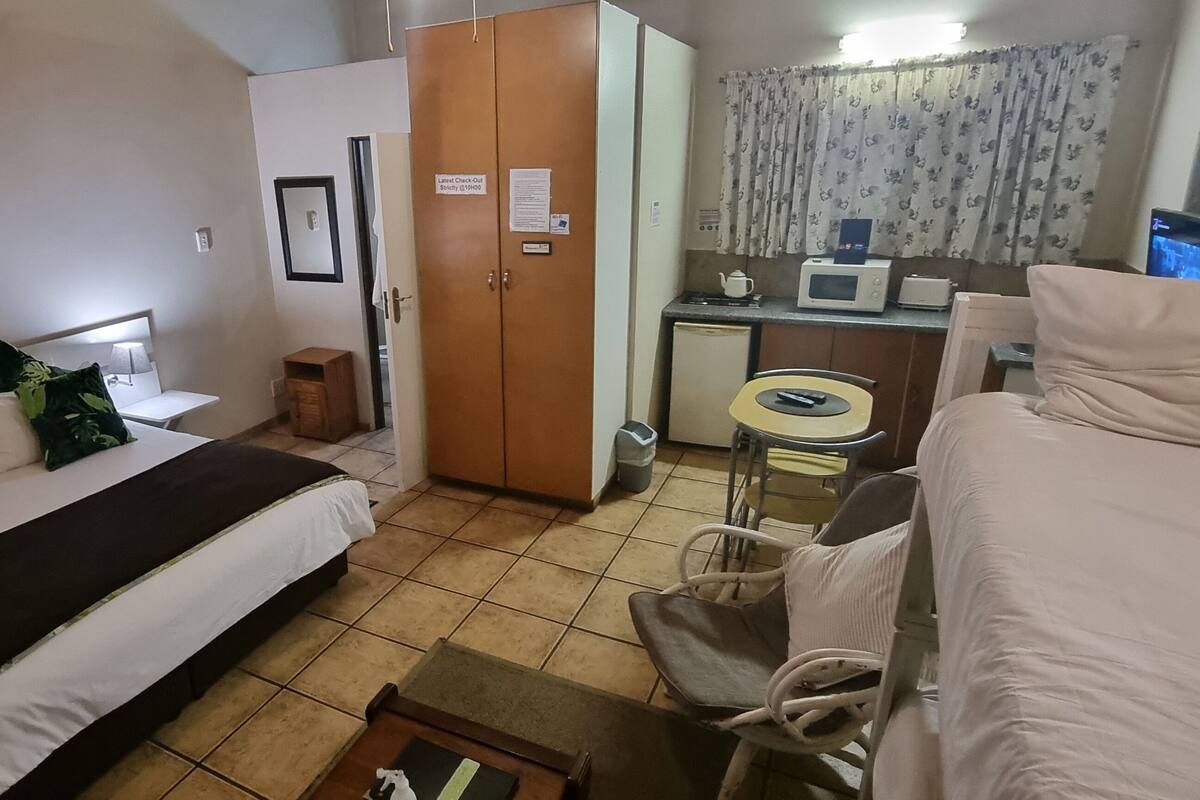 A hotel room with a bed, a desk with a computer, a small kitchenette, and a wardrobe.