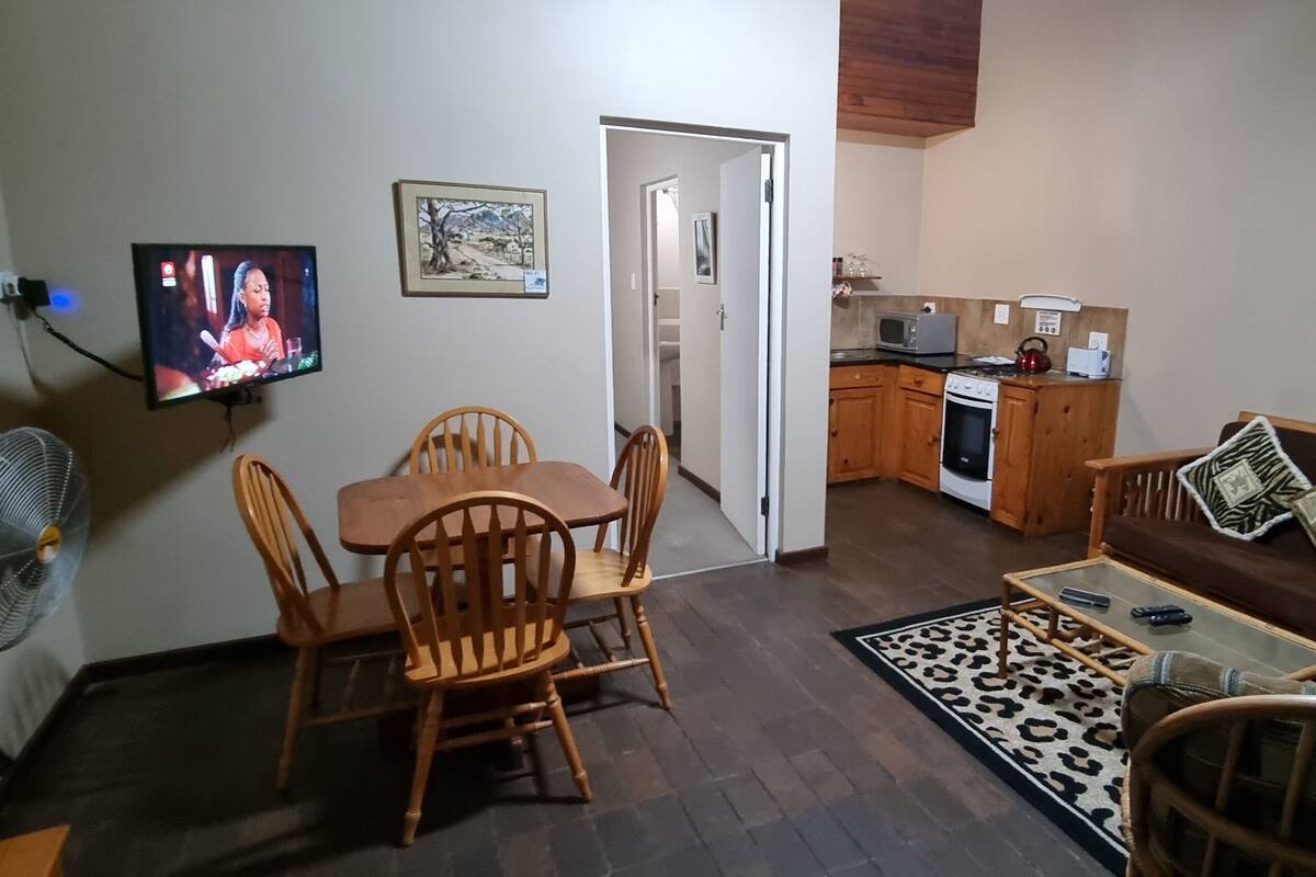 A living room with a TV, dining table, chairs, a sofa, and a kitchen area with appliances.