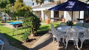 A patio with a pool, white metal chairs, and a table under a blue umbrella.