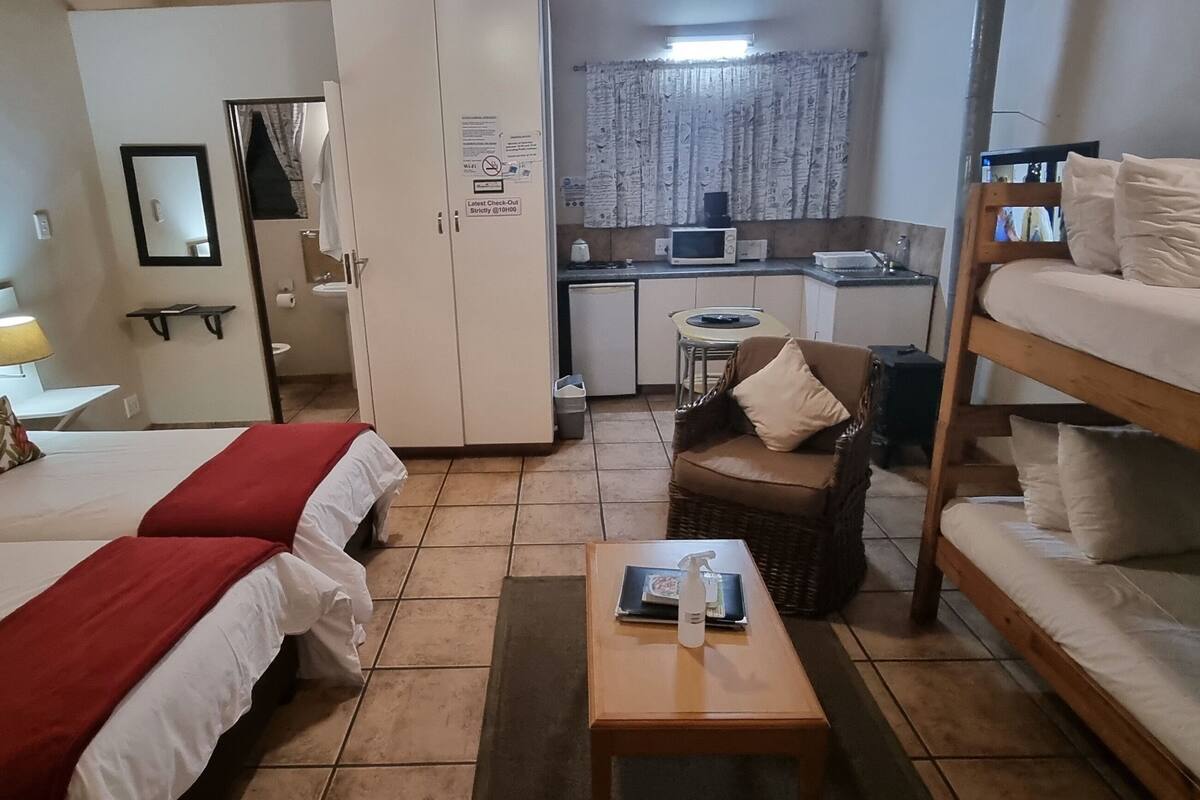 A hotel room with two beds, a small kitchenette, a bathroom, and a dining area.