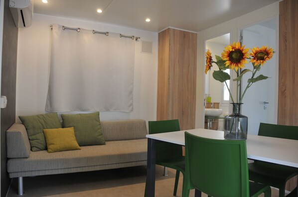 A modern living room with a sofa, green chairs, a dining table, and a vase with sunflowers.