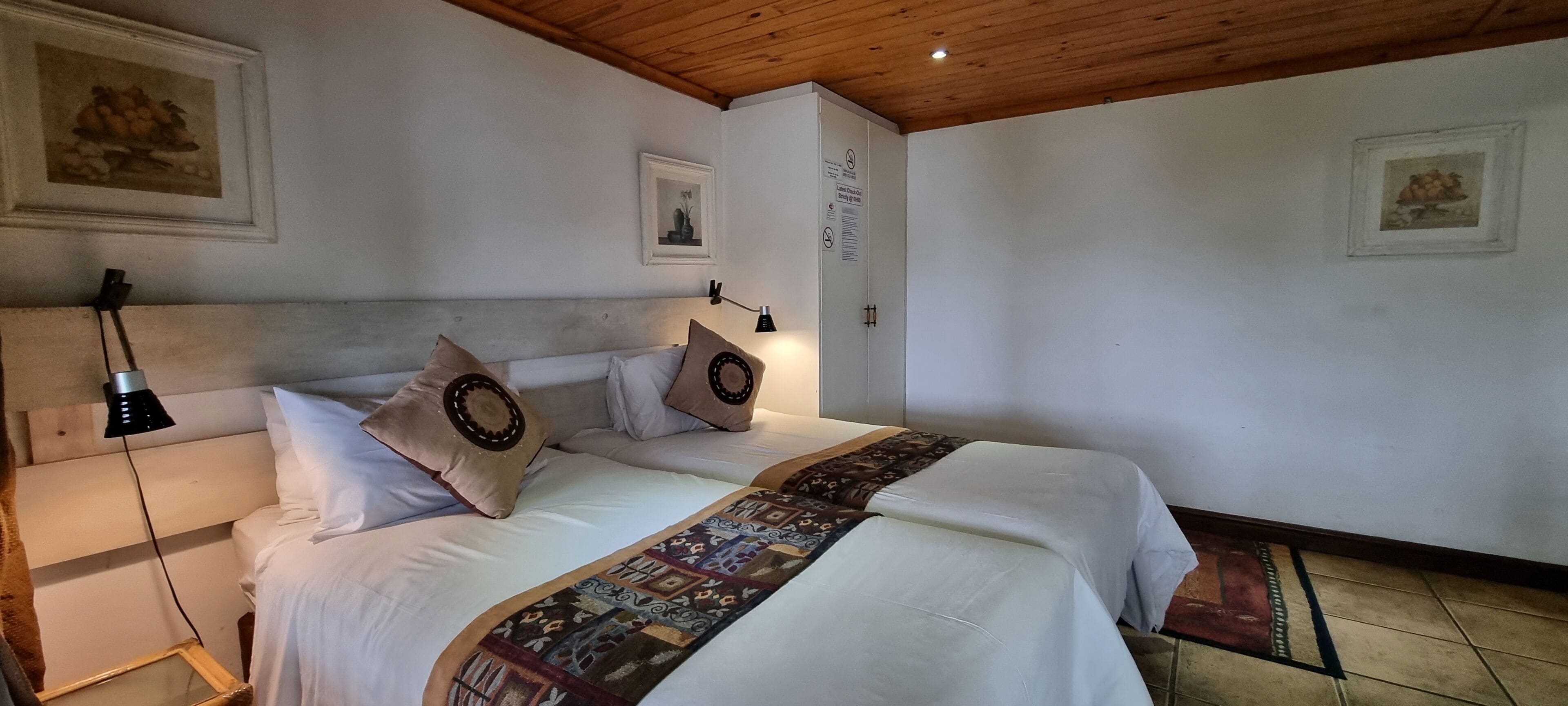 A neatly made bed with a patterned bedspread, two pillows, and a headboard. There is a nightstand with a lamp and a framed picture on the wall.