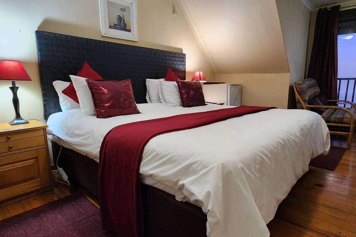 Ett hotellrum med en stor säng, två sänglampor, ett litet träbord, ett skrivbord, en stol och en balkong med utsikt.