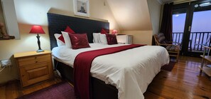 A hotel room with a large bed, two bedside lamps, a wooden nightstand, a small desk, a chair, and a balcony with a view. - Lagoon Lodge (Knysna)
