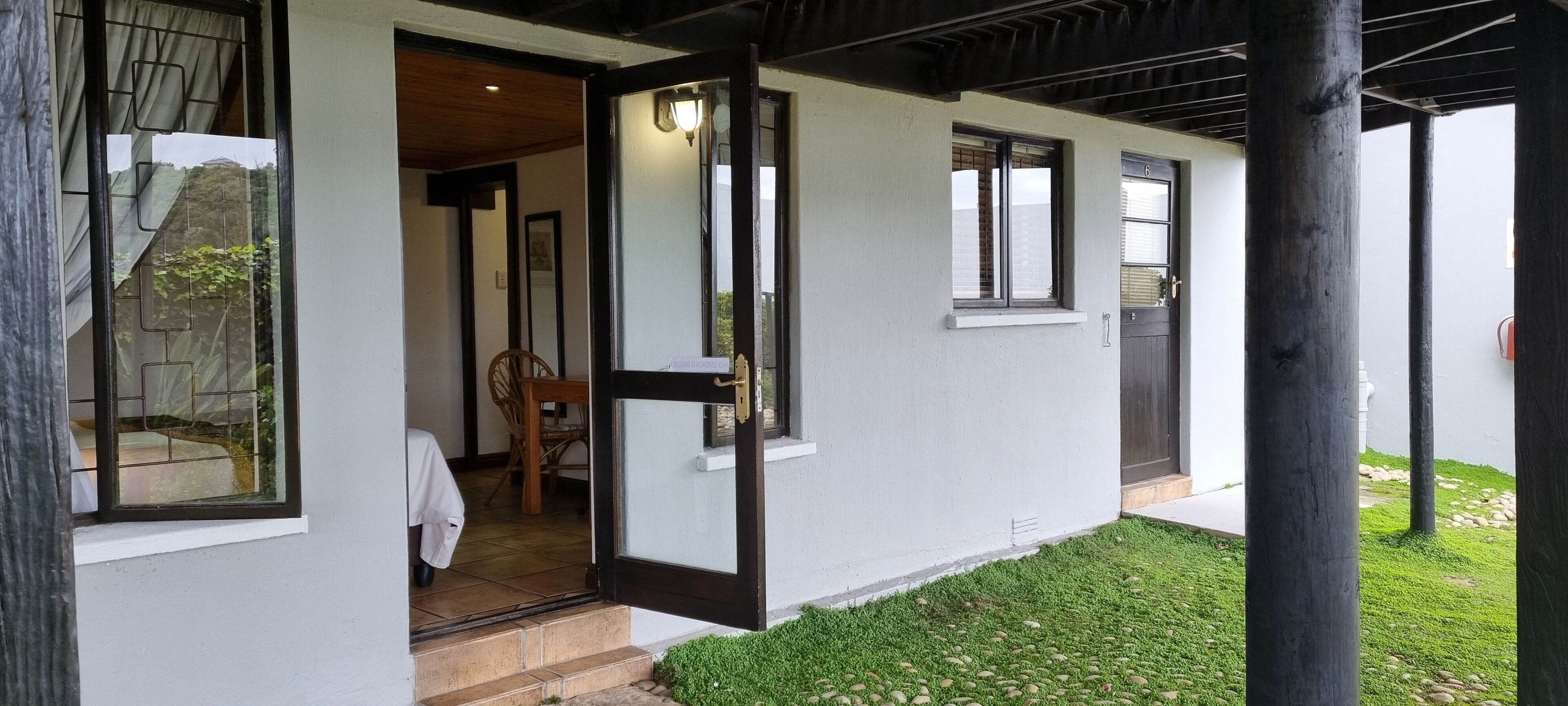 A house with a wooden porch, a dining area with a table and chairs, and a small window.