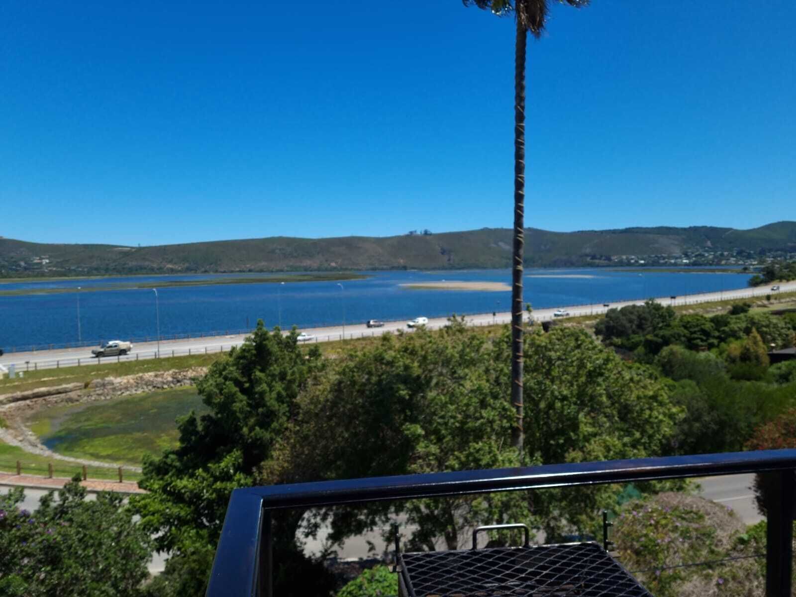A coastal view with a road, a body of water, and hills in the background.