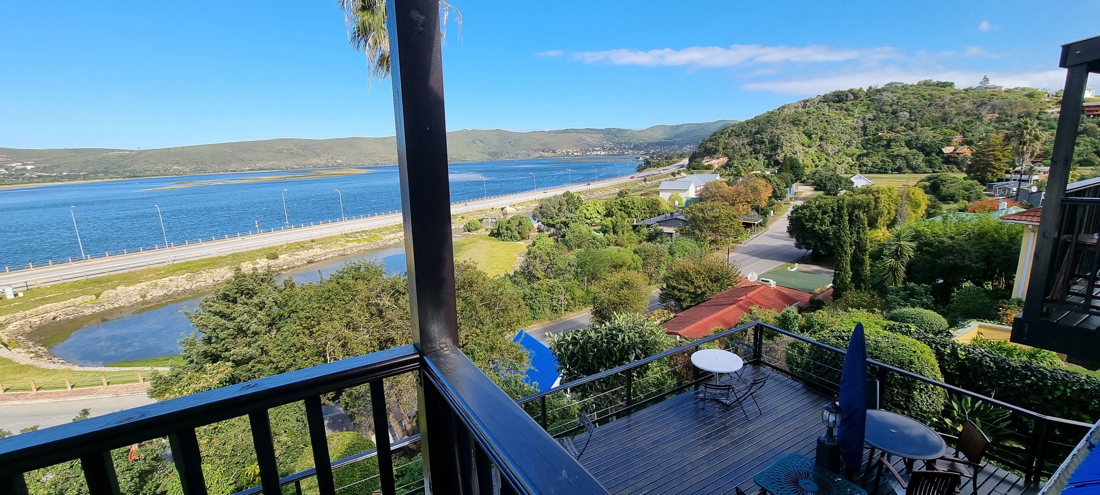 Un balcon donnant sur une zone côtière, avec vue sur une route, un pont et une étendue d’eau.