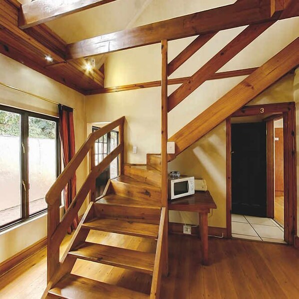 A wooden staircase leading to a landing with a microwave on a small table. - Lagoon Lodge (Knysna)