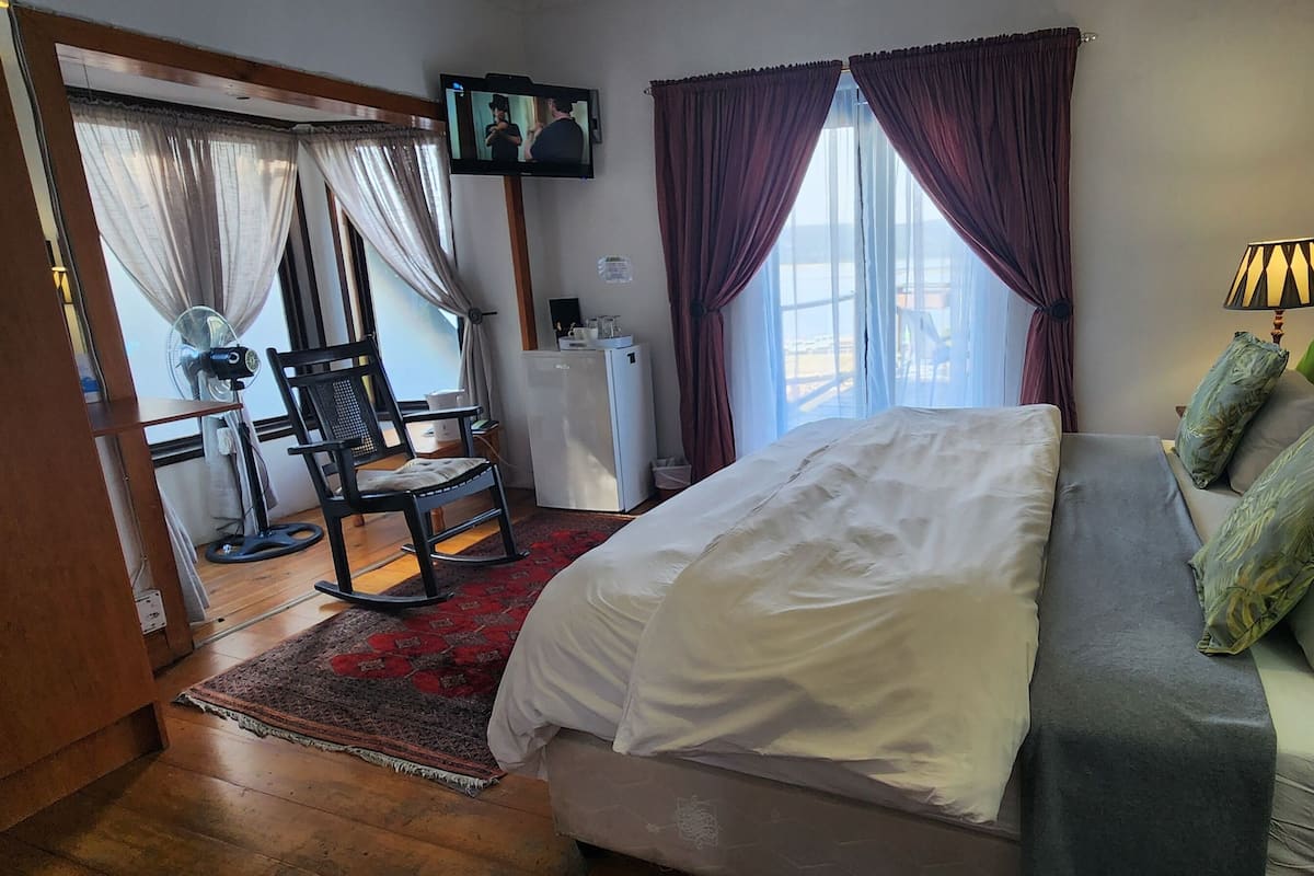 Ett hotellrum med en säng, en tv som är monterad på väggen, ett skrivbord med en stol och ett fönster med gardiner.
