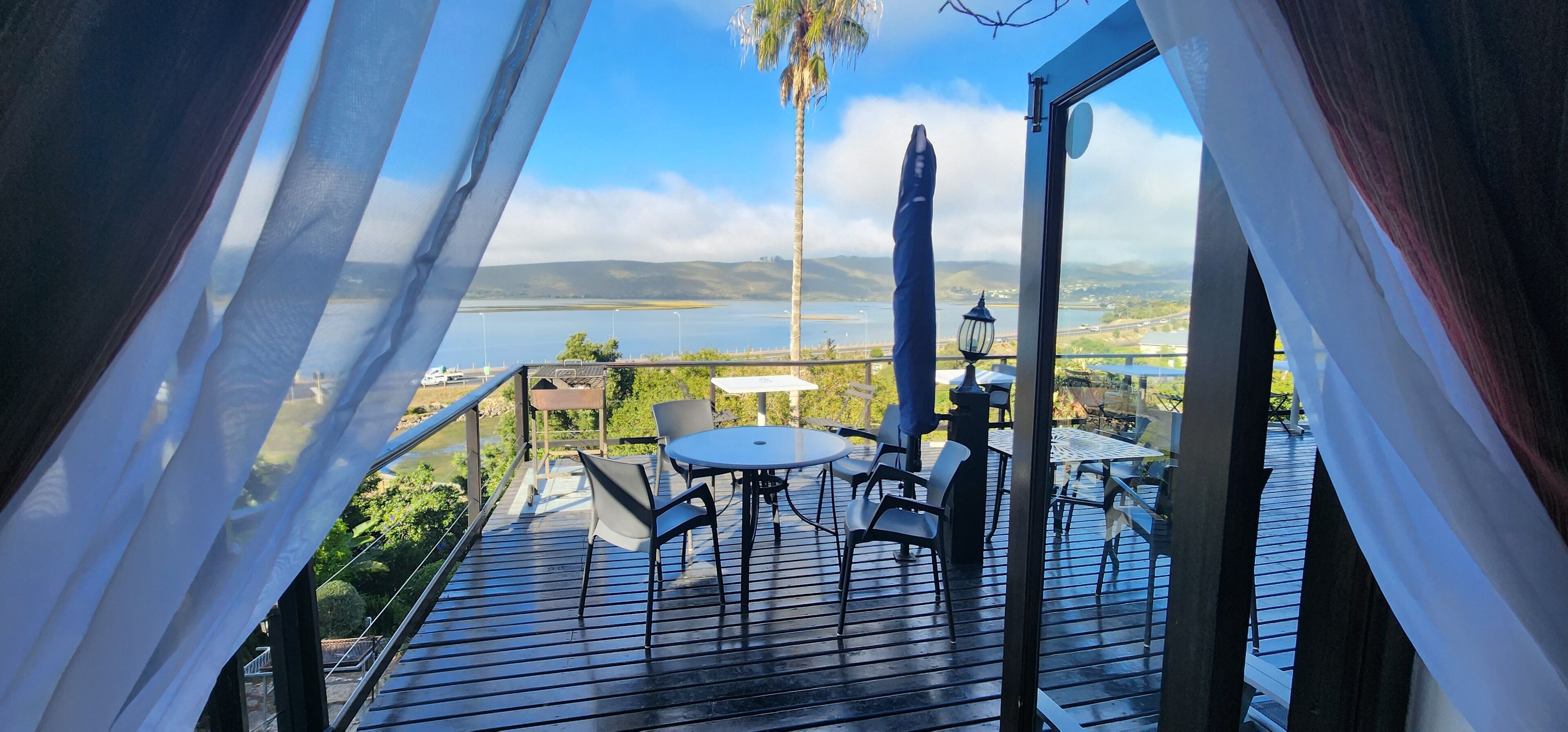 A deck with a table and chairs, overlooking a body of water and distant hills.