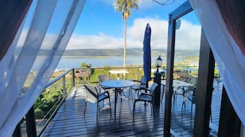 Una terraza con mesa y sillas, con vista a un cuerpo de agua y colinas distantes.