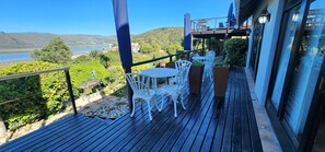 A balcony with white outdoor furniture, a view of a lake, and a distant bridge. - Lagoon Lodge (Knysna)