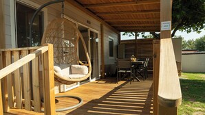Une terrasse en bois avec un fauteuil suspendu, une table et des chaises.