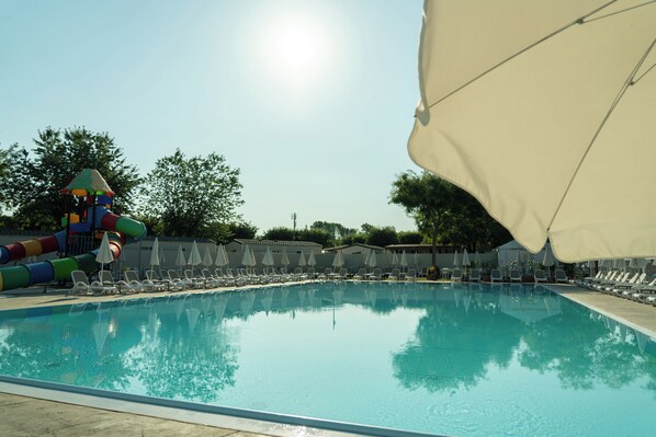 A swimming pool with lounge chairs and umbrellas, a water slide, and a clear sky. - Butterfly Camping Village (Peschiera del Garda)