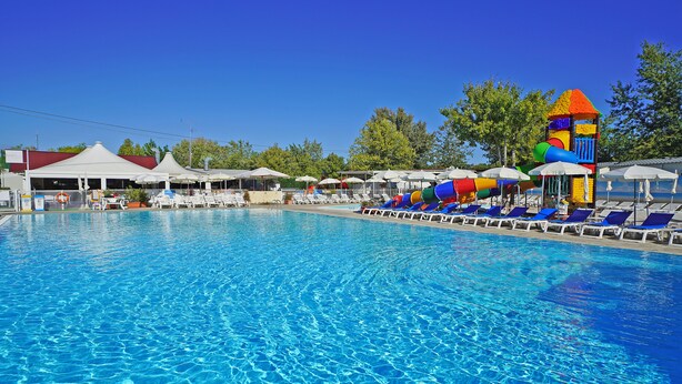 Une piscine entourée d’arbres et d’immeubles, avec des chaises longues et des parasols.