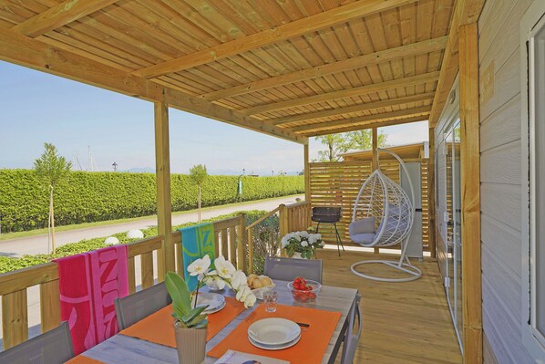 Un espacio al aire libre cubierto con una terraza de madera, un sillón colgante, una mesa dispuesta para comer y vistas a un viñedo.