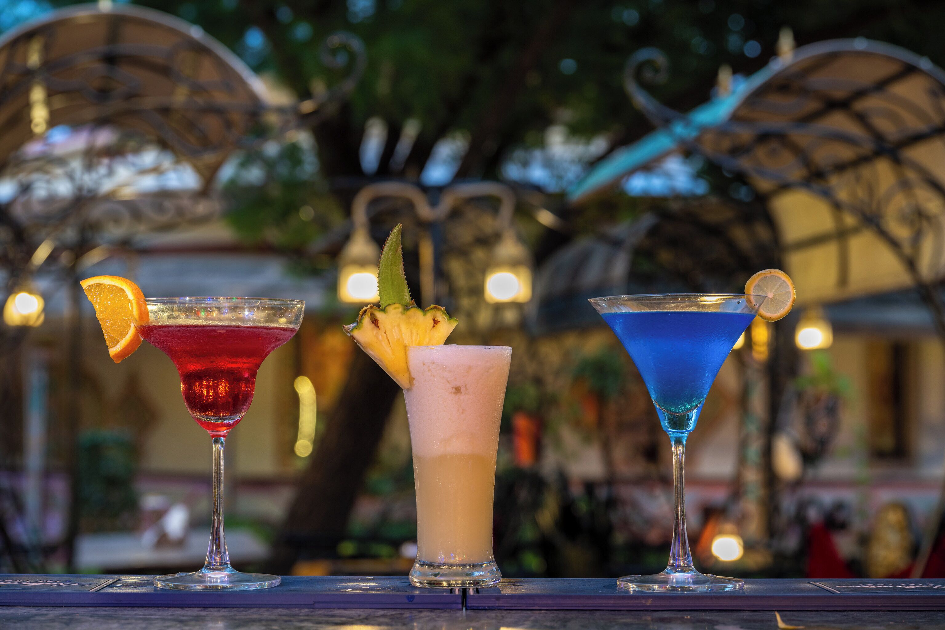 Three cocktails on a bar counter with a blurred outdoor background.