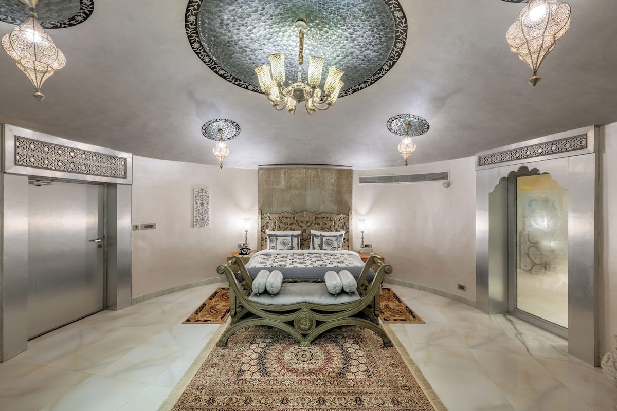 A spacious bedroom with a large bed, ornate ceiling chandelier, and decorative wall panels.