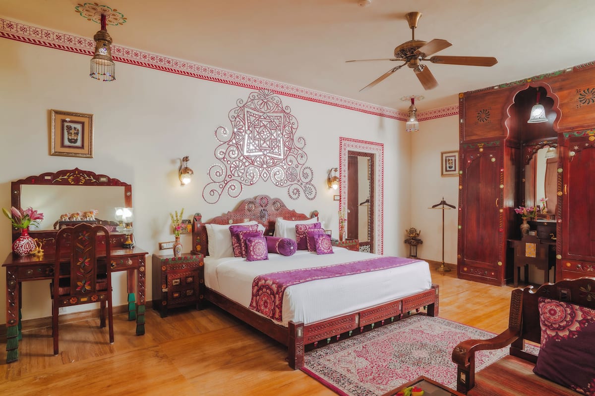 A traditional room with a bed, wooden furniture, a ceiling fan, and decorative wall patterns.