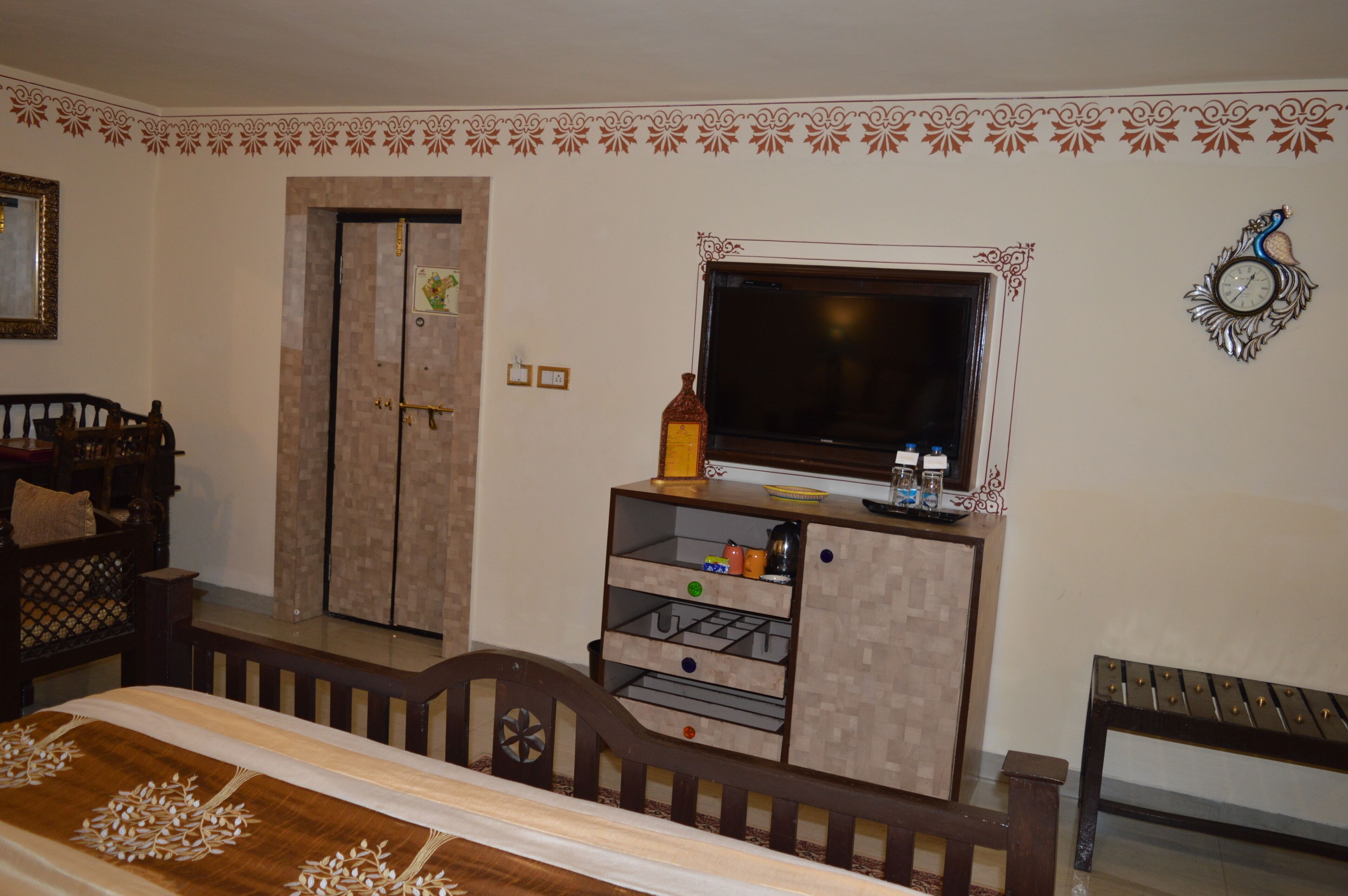 A bedroom with a bed, a TV on a wooden stand, a wardrobe, and a decorative clock on the wall.