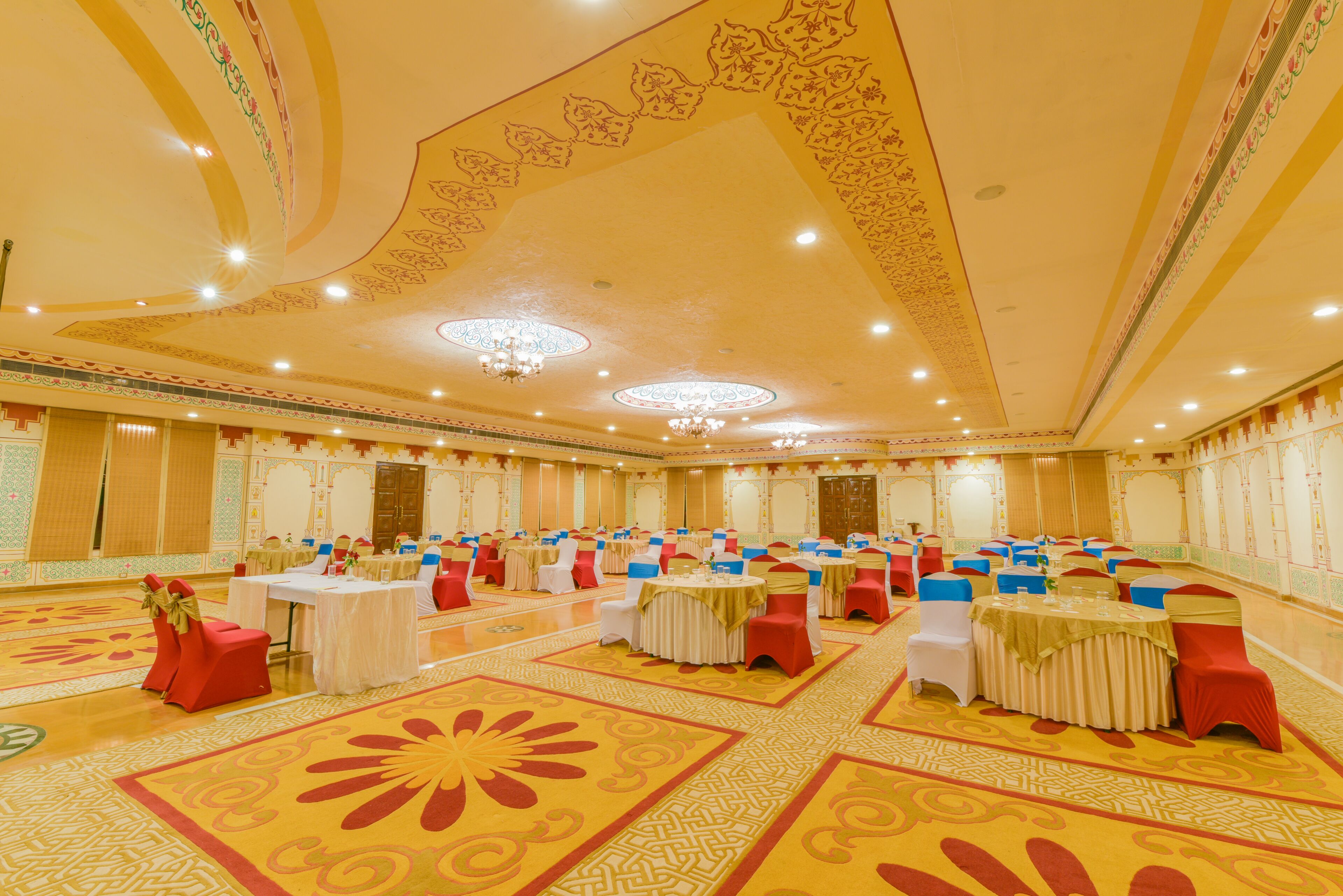 A banquet hall with round tables, red and white chairs, and patterned carpet.
