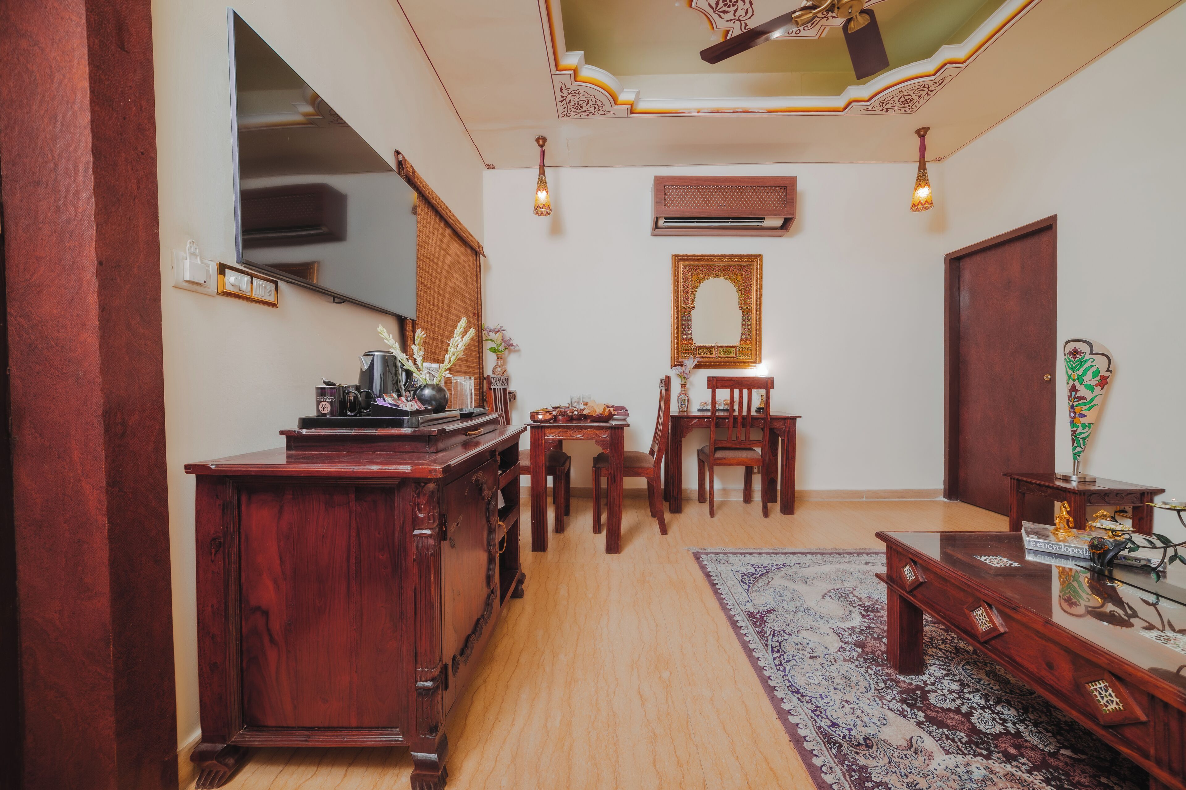 A traditional room with a wooden desk, a mirror, a patterned rug, and a ceiling with ornate design.