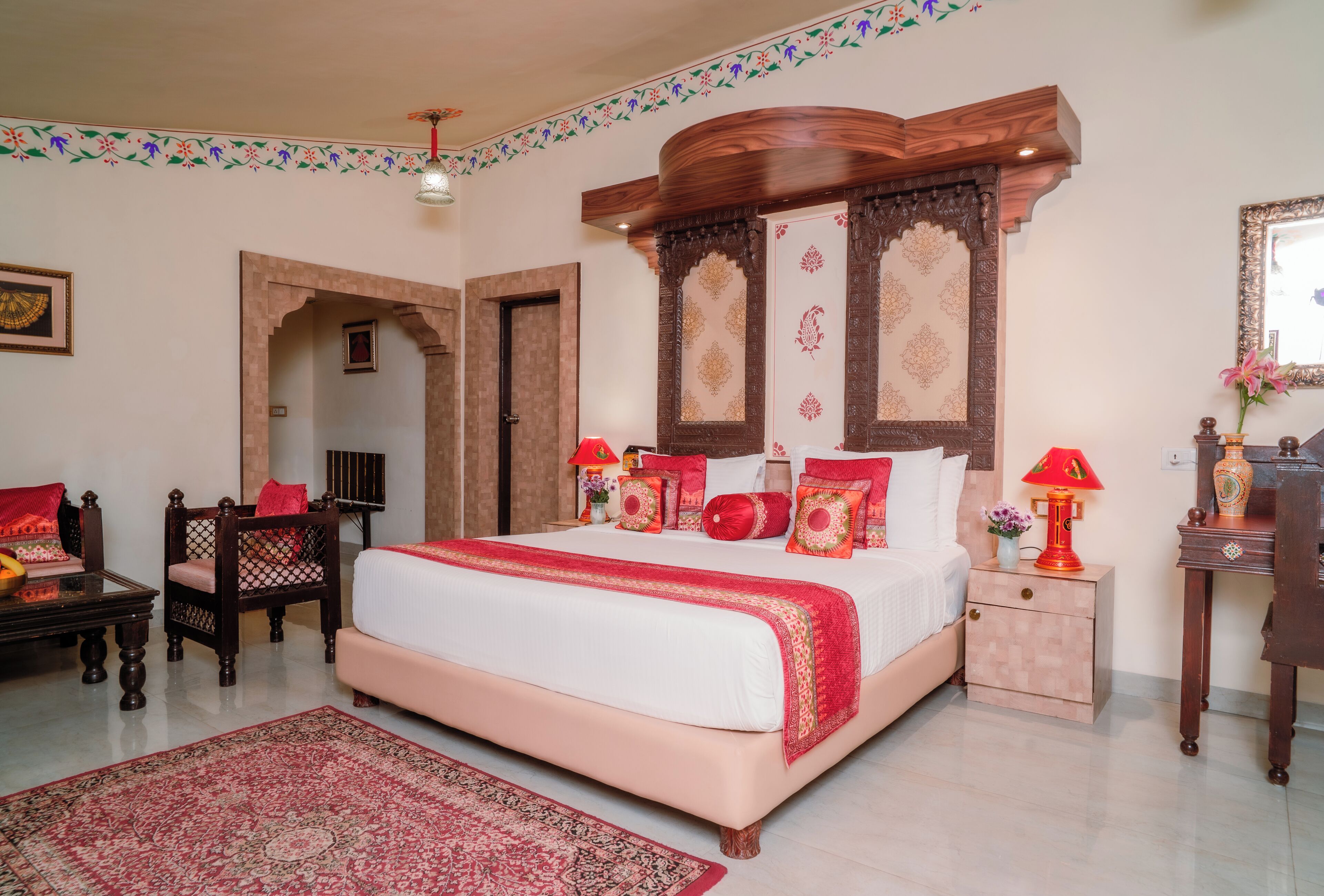 A bedroom with a large bed, wooden headboard, a nightstand, a chair, and a small table with a lamp.