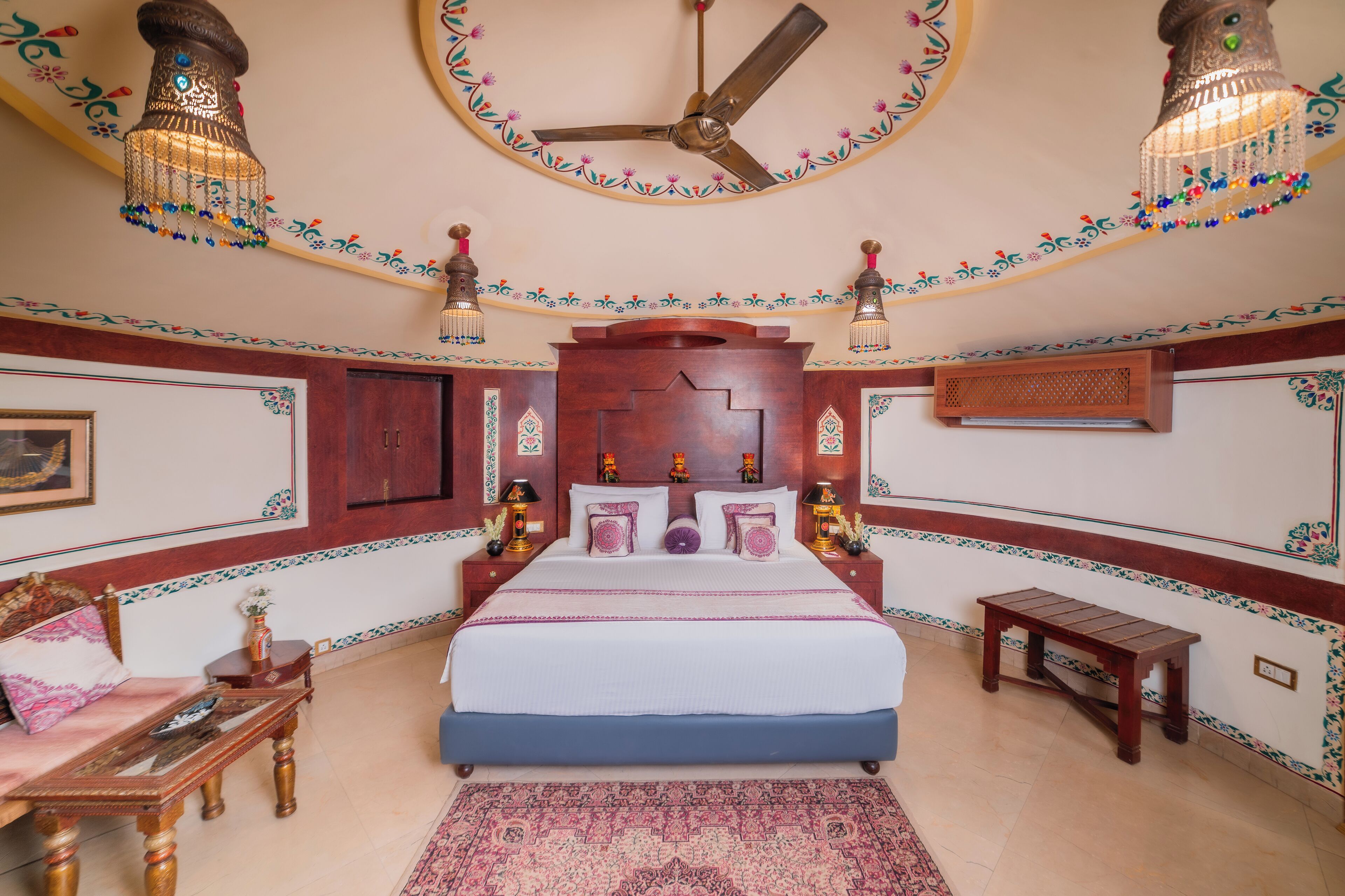 A bedroom with a large bed, a ceiling fan, decorative wall lamps, and a wooden nightstand.