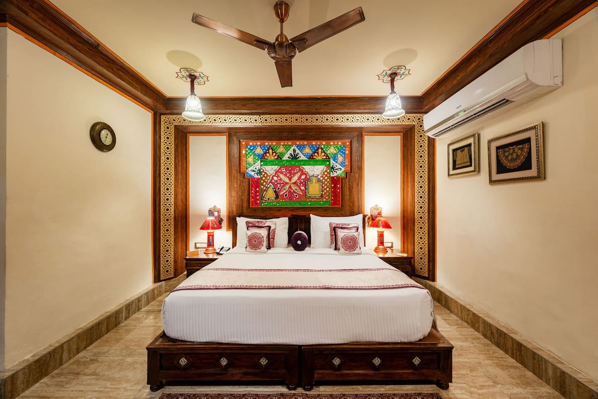 A spacious bedroom with a large bed, wooden headboard, decorative wall panels, and a ceiling fan.