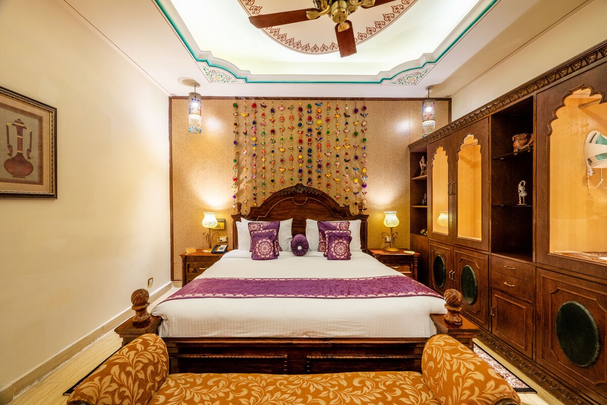Une chambre d’hôtel élégamment aménagée, dotée d’un grand lit, d’une tête de lit en bois sculptée et d’une décoration murale.