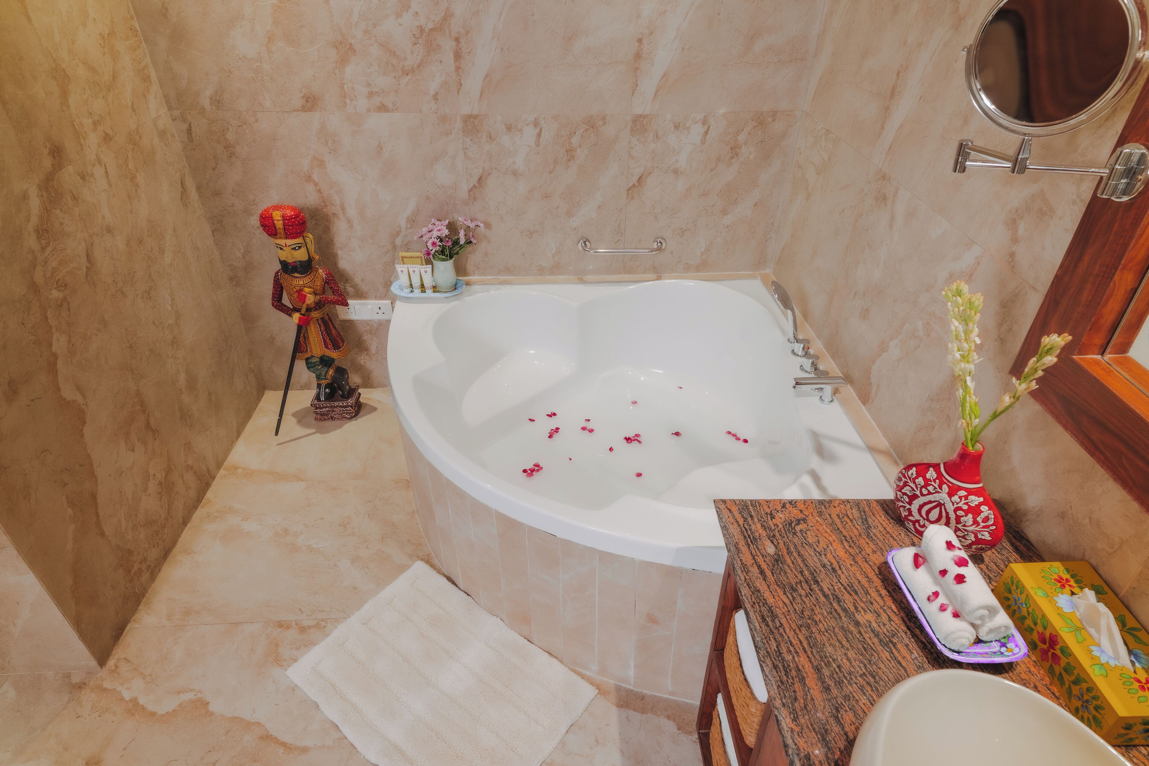 A bathroom with a large bathtub, a wooden vanity, a mirror, and a decorative statue.