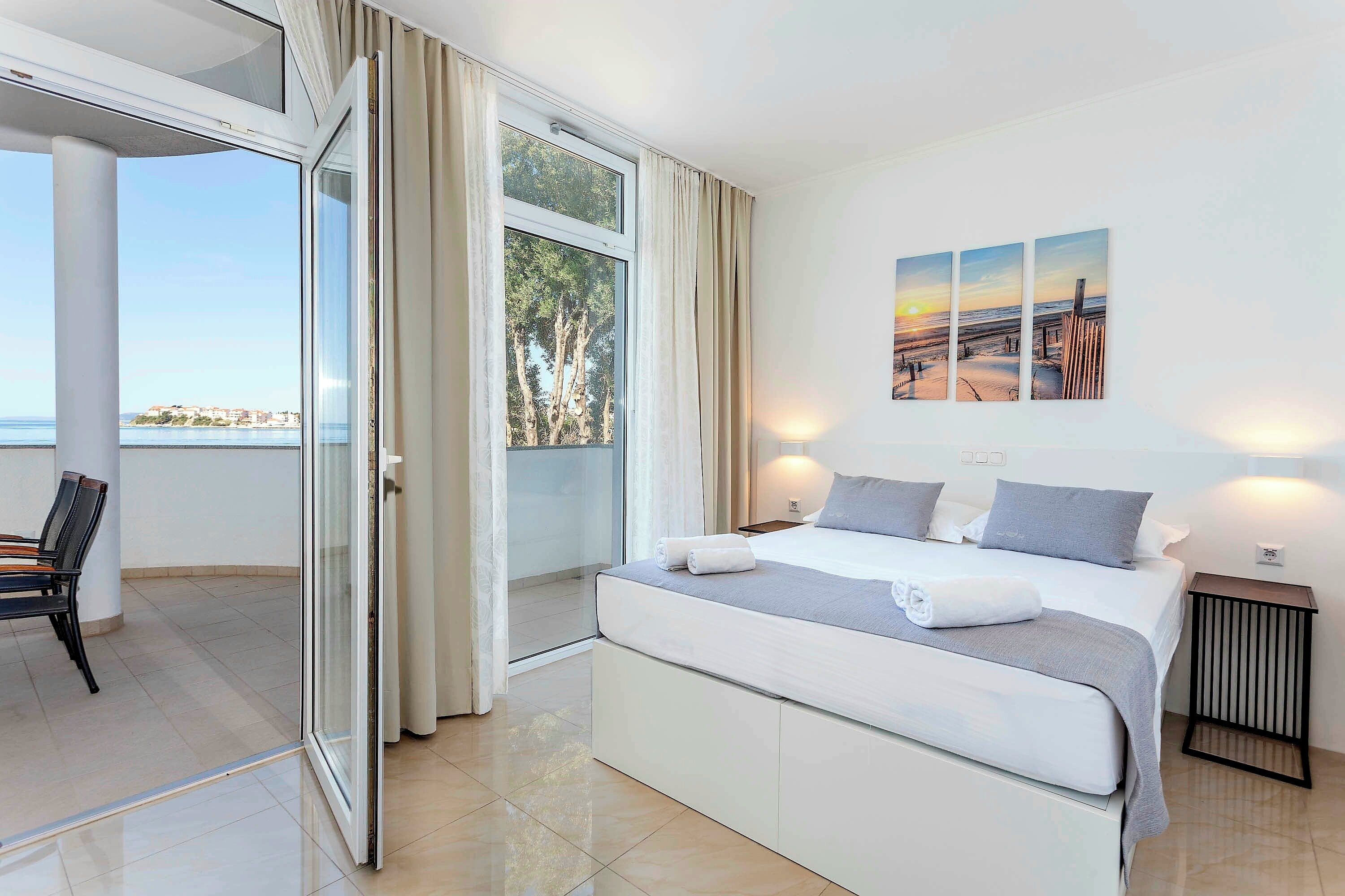 Une chambre à coucher moderne, avec un lit, une table de chevet et une vue sur la mer par une grande fenêtre.