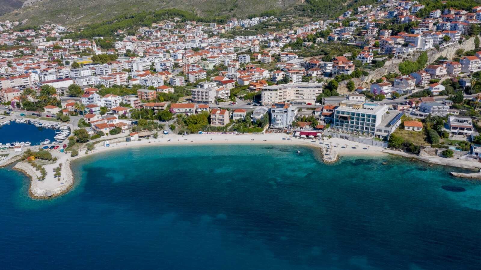 Luftaufnahme einer Küstenstadt mit Strand, Gebäuden und einem Yachthafen.