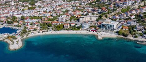 An aerial view of a coastal town with a beach, buildings, and a marina.
