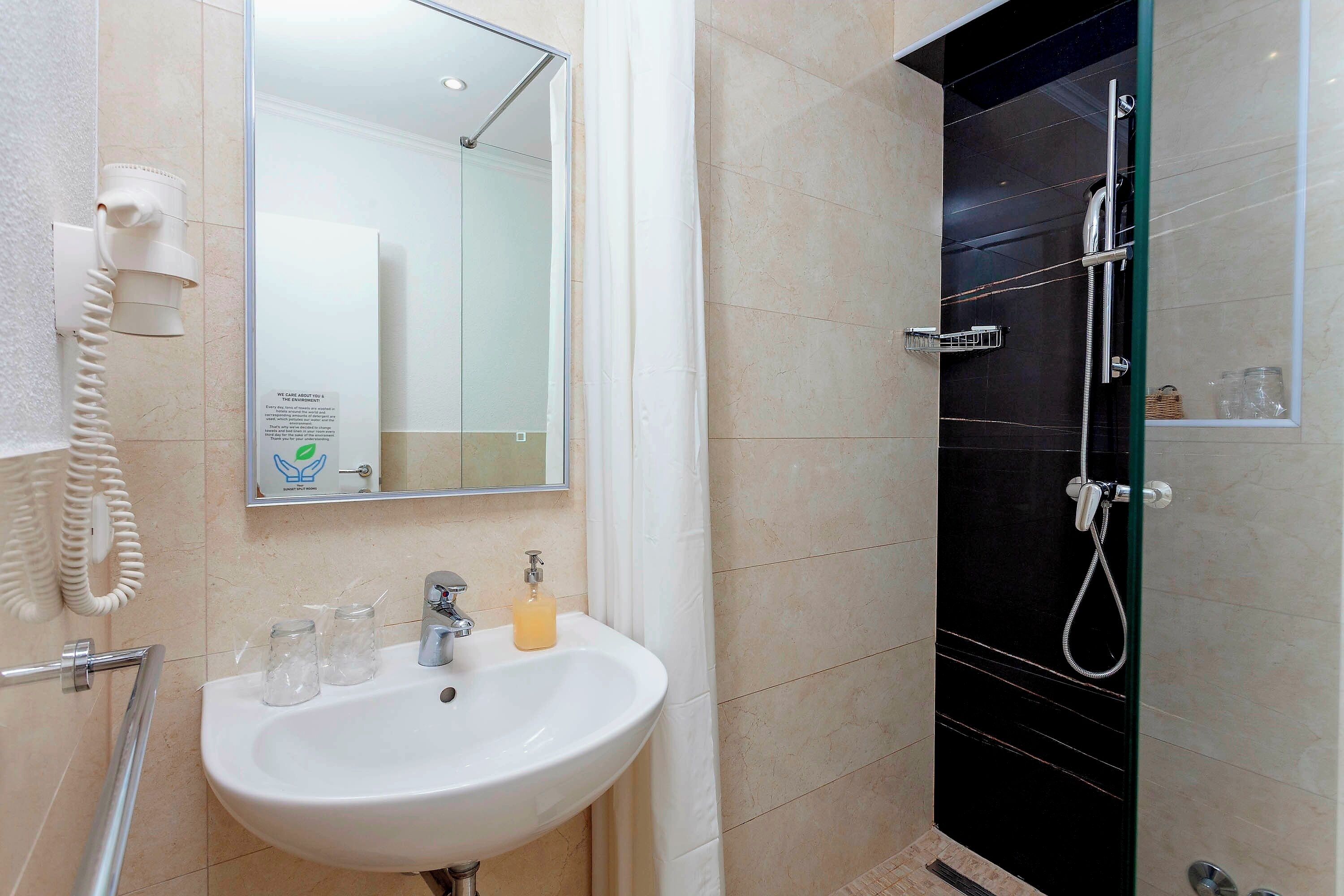 A bathroom with a white sink, a mirror, a glass shower enclosure, and a telephone.