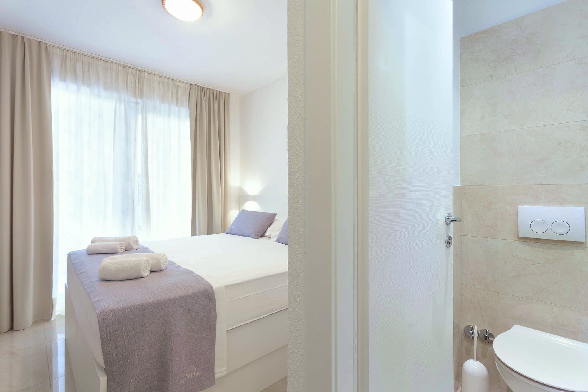 A hotel room with a bed, a bedside table with towels, a bathroom with a toilet and sink.