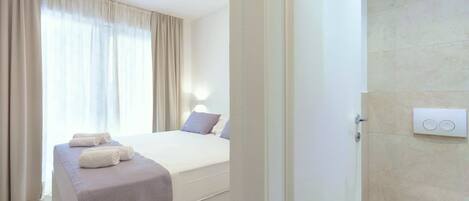 A hotel room with a bed, a bedside table with towels, a bathroom with a toilet and sink.