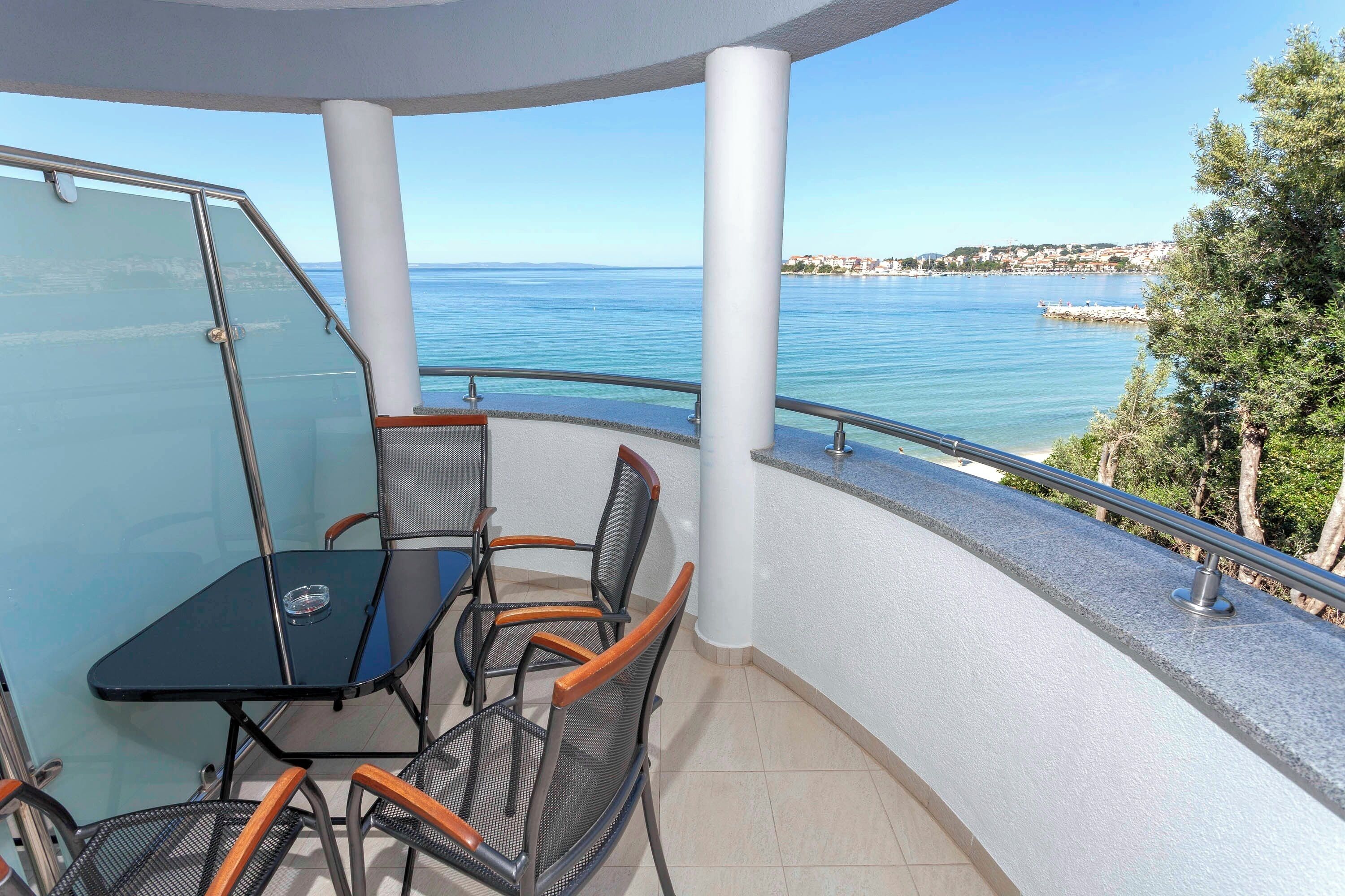 En balkon med et glasbord og stole, havudsigt og gelænder.