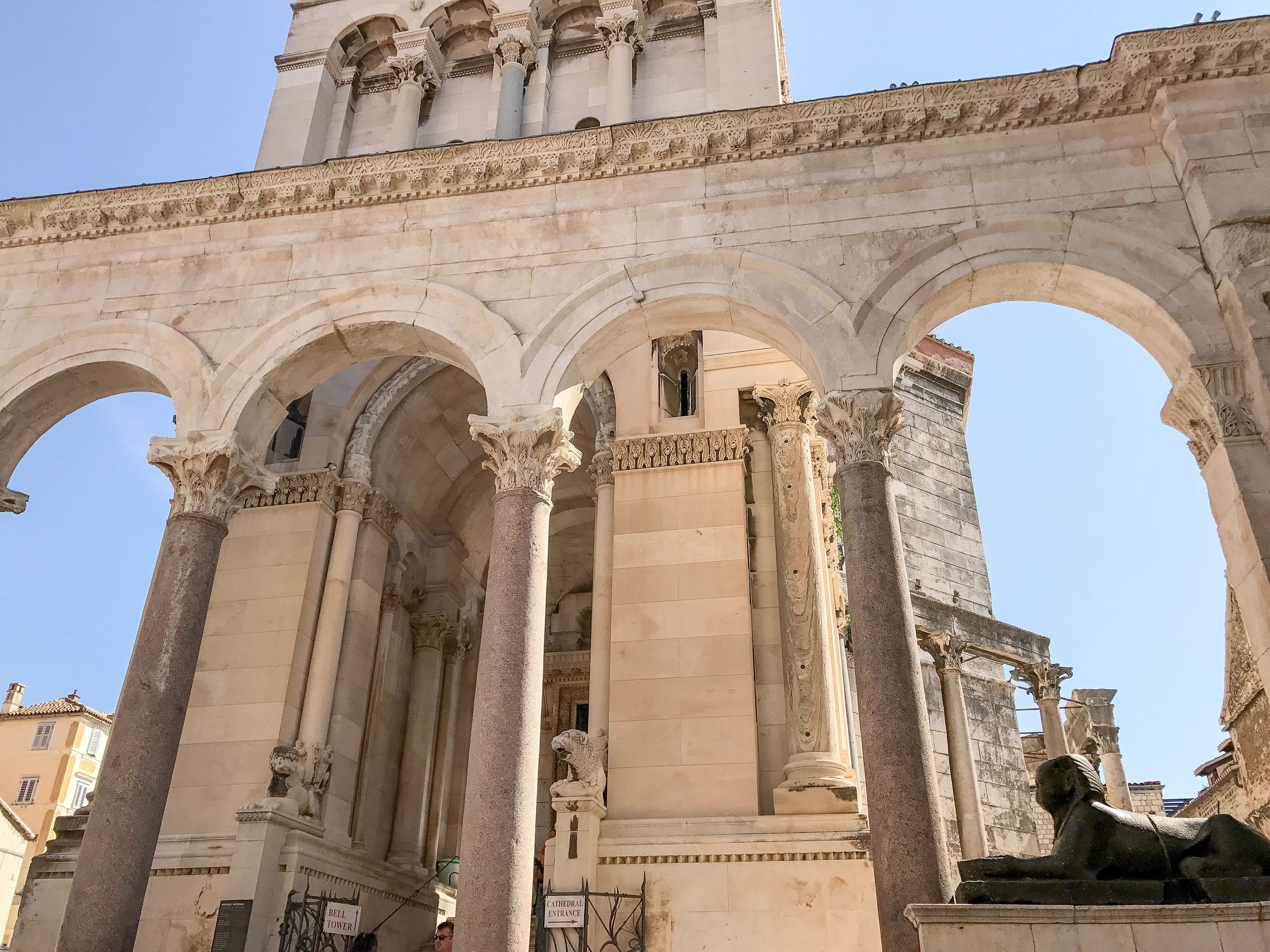 Una antigua estructura arquitectónica con múltiples arcos y columnas, que presenta una estatua de una esfinge.