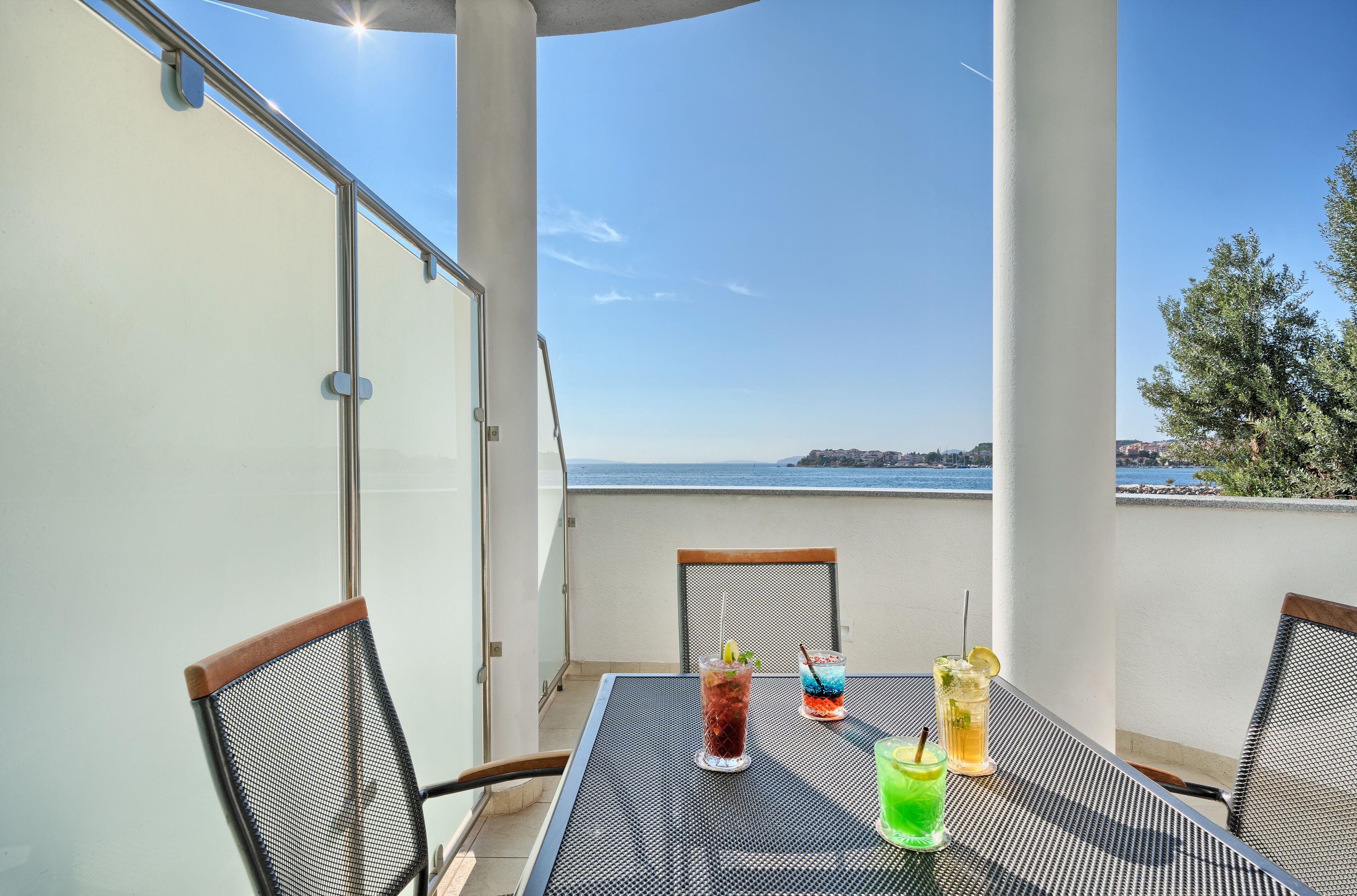 Un balcone con un tavolo apparecchiato per bevande, affacciato su una vista panoramica del mare e della costa.