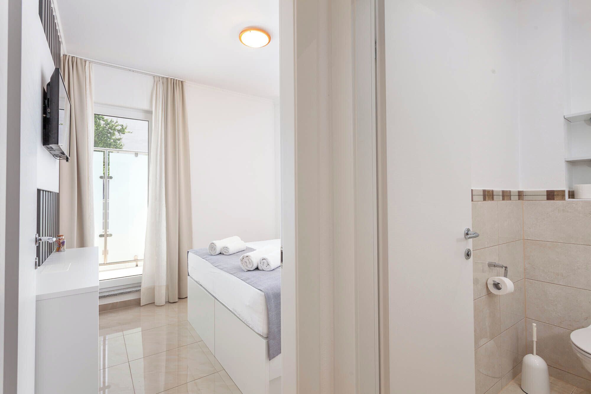 A hotel room with a bed, a bathroom with a toilet and sink, and a window with curtains.
