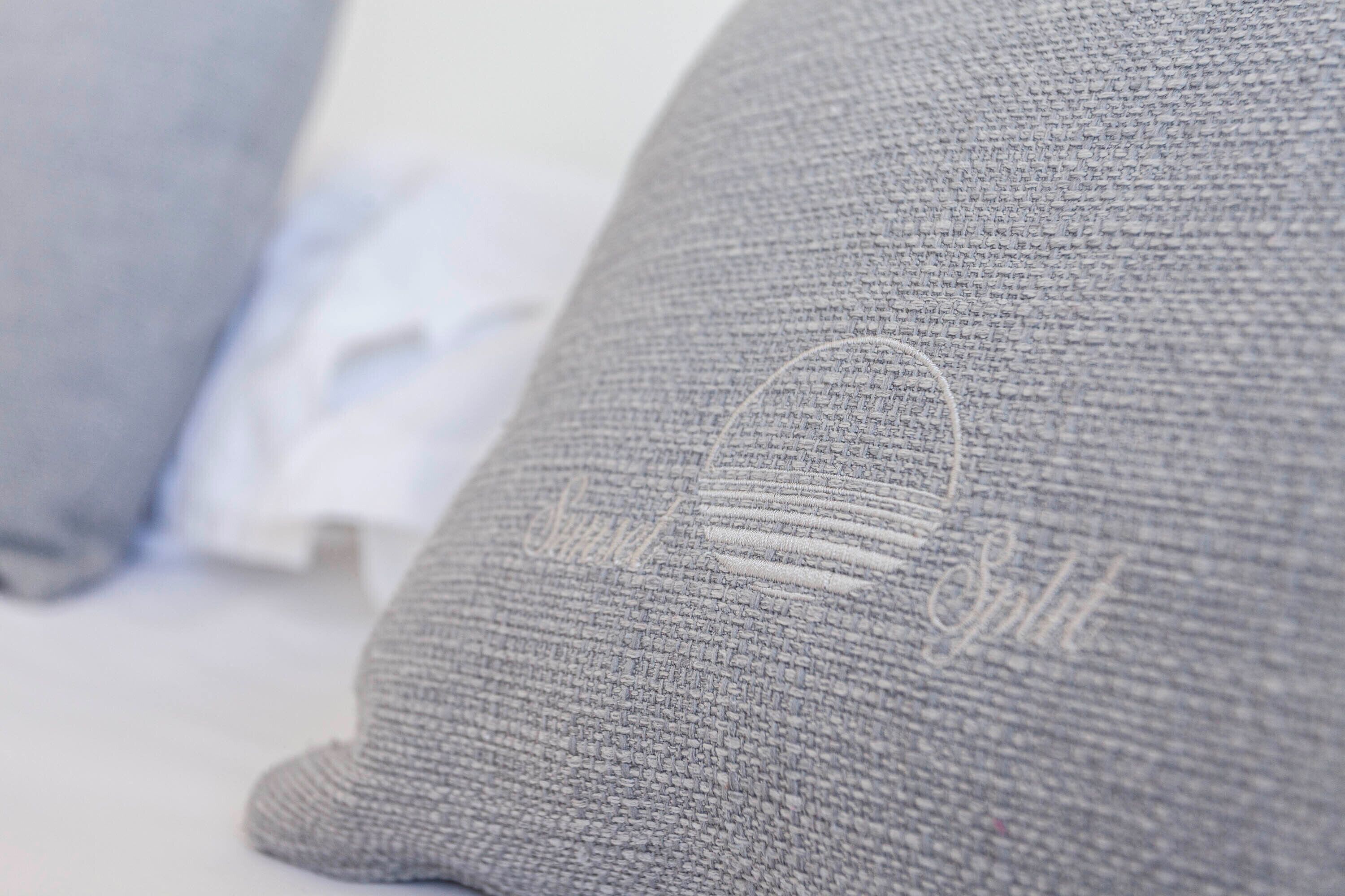 A close-up of a grey knitted pillow with a circular embroidered design.