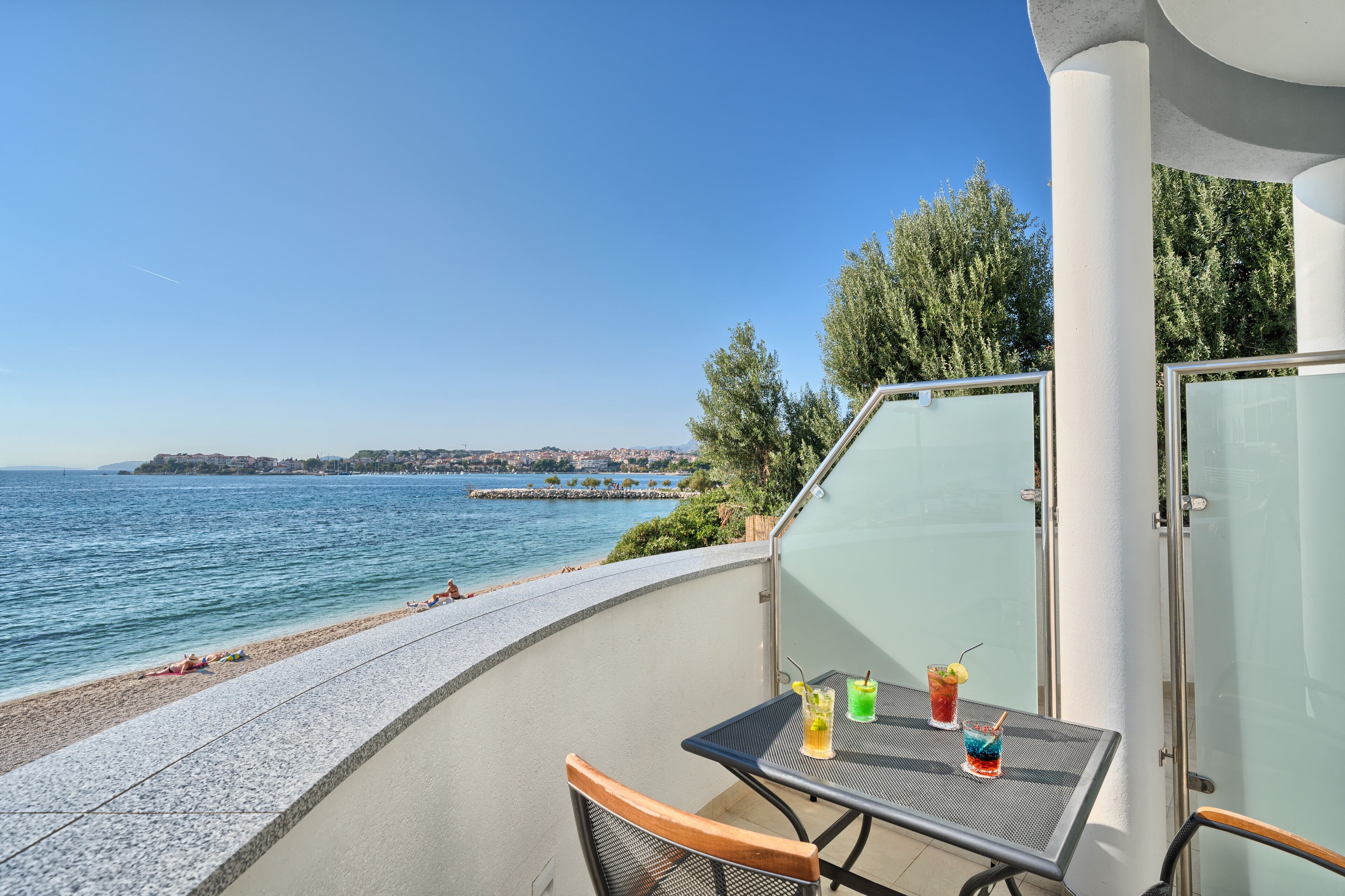 Ein Balkon mit Tisch und Stühlen mit Blick auf einen Strand und das Meer.